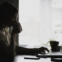 一位短发女性在书桌前整理读者来信，笔记本电脑屏幕泛着暖光，旁边贴着写满问题的便利贴，氛围亲切自然